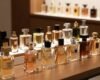 A stylish, elegant display of men's perfumes, showcasing both imported and domestic brands, arranged on a sleek wooden table. In the foreground, a variety of intricately designed glass bottles with unique shapes and colors, reflecting light softly. In the middle ground, a subtle differentiation between the imported and national perfumes can be seen, perhaps with a small flag or emblem subtly incorporated next to each type to signify their origins. The background features a softly blurred shelf with more perfume choices, enhancing a luxurious atmosphere. The scene is lit with warm, inviting lighting that creates a sophisticated, intimate mood, suitable for an evening occasion. The angle is slightly above eye level, giving a clear view of the bottles while maintaining an air of elegance and allure.
